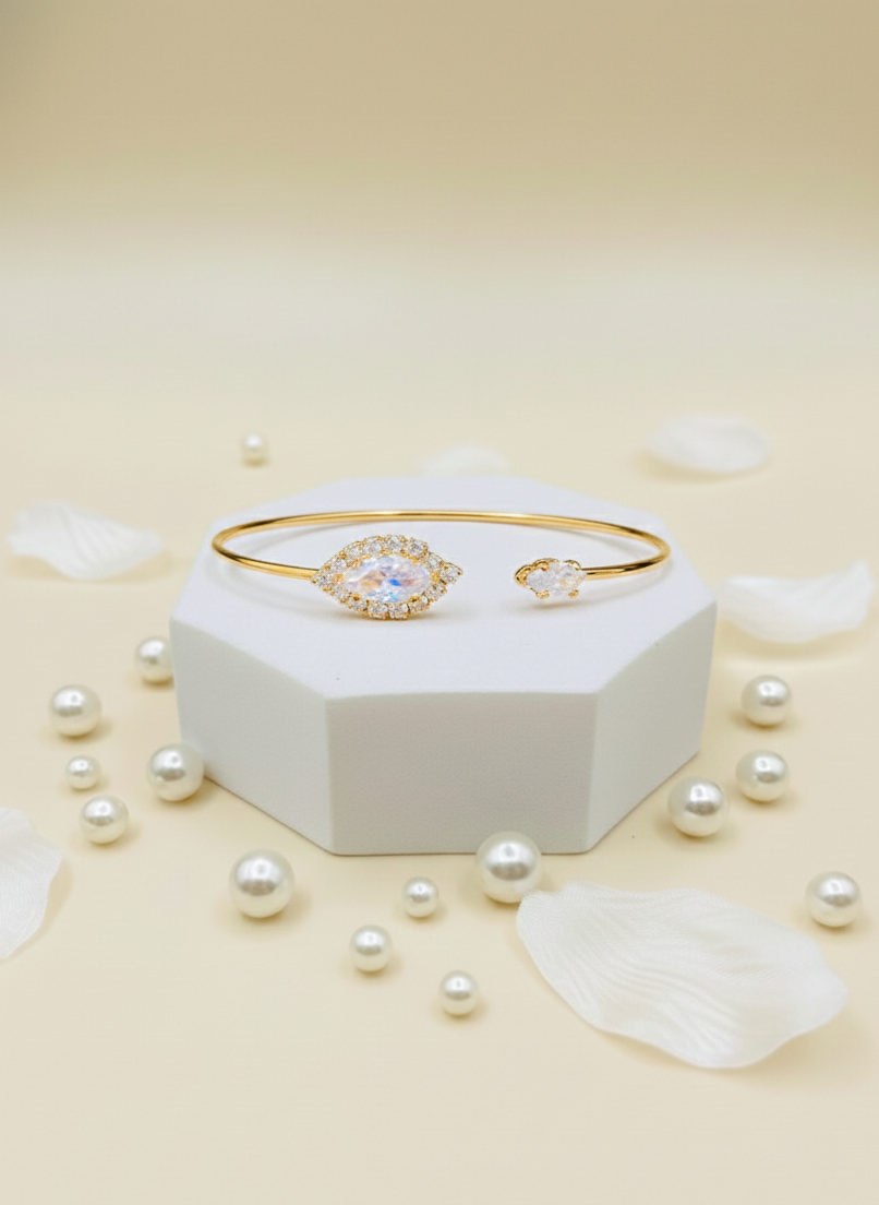 Gold bracelet with a heart-shaped clasp on a white box with scattered pearls on a beige background