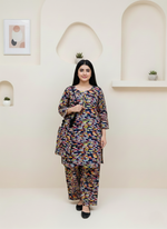 Woman wearing a colorful outfit standing against a white wall with decorative elements.
