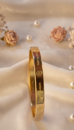Gold bracelet with engraved text on a soft white background with pearls and flowers.