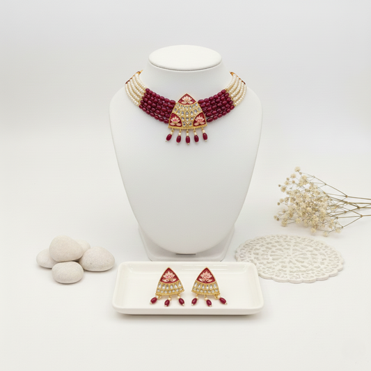 Decorative necklace with red beads on a white stand, accompanied by earrings on a small tray.