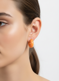 Close-up of a person wearing orange hoop earrings with a neutral background