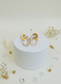 Gold and white earrings on a white jewelry box with decorative elements.