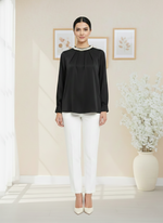 Woman wearing a black blouse and white pants in a minimalistic room.