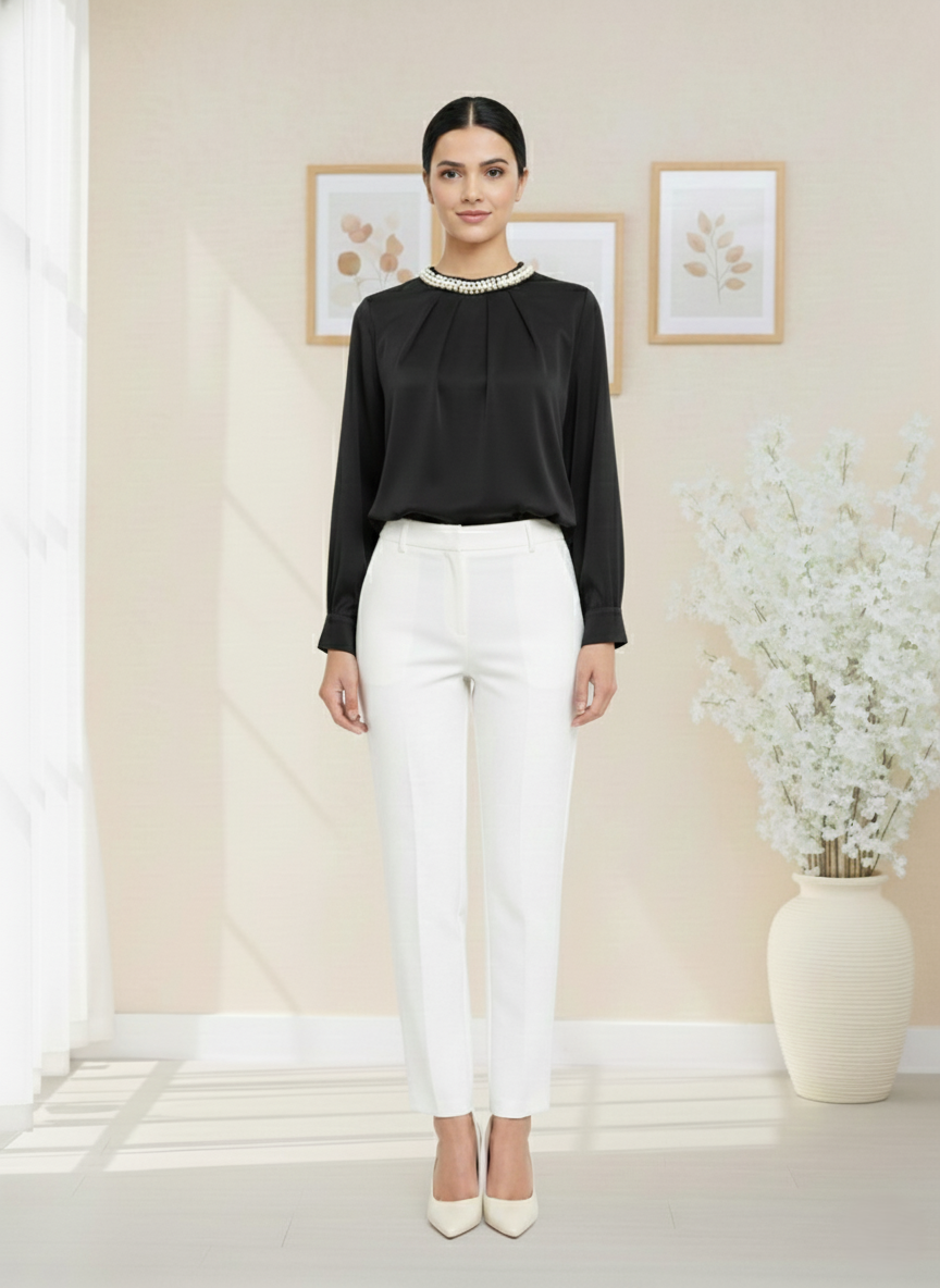 Woman wearing a black blouse and white pants in a room with decorative elements.