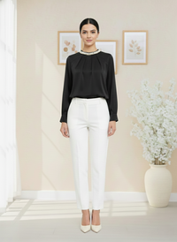 Woman wearing a black blouse and white pants in a room with decorative elements.