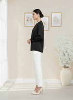 Woman in black top and white pants standing in a room with light-colored walls and decor.