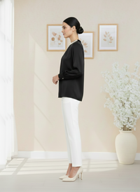 Woman in black top and white pants standing in a room with light-colored walls and decor.