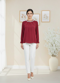 Woman wearing a red blouse and white pants in a room with decorative elements.