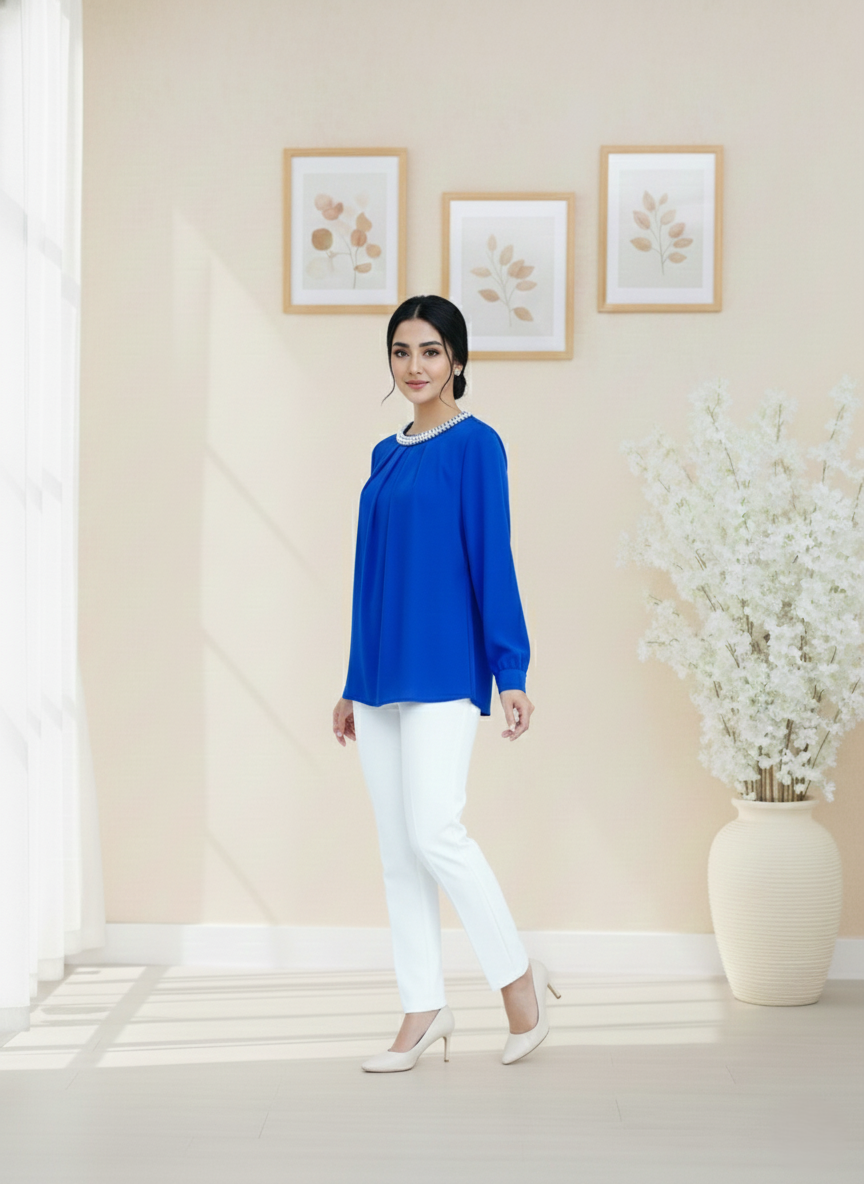 Woman in a blue top and white pants standing in a room with light-colored walls and decor.