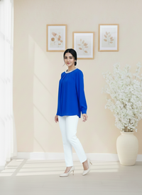 Woman in a blue top and white pants standing in a room with light-colored walls and decor.