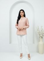 Woman wearing a pink top and white pants standing in front of a white archway.