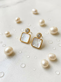 Gold earrings with square母贝片 surrounded by pearls on a light background