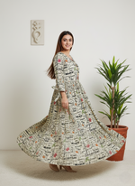 Woman wearing a long, patterned dress standing in a room with a plant and wall art.