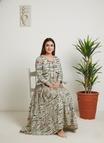 Woman in a floral dress sitting on a chair next to a potted plant against a white wall.