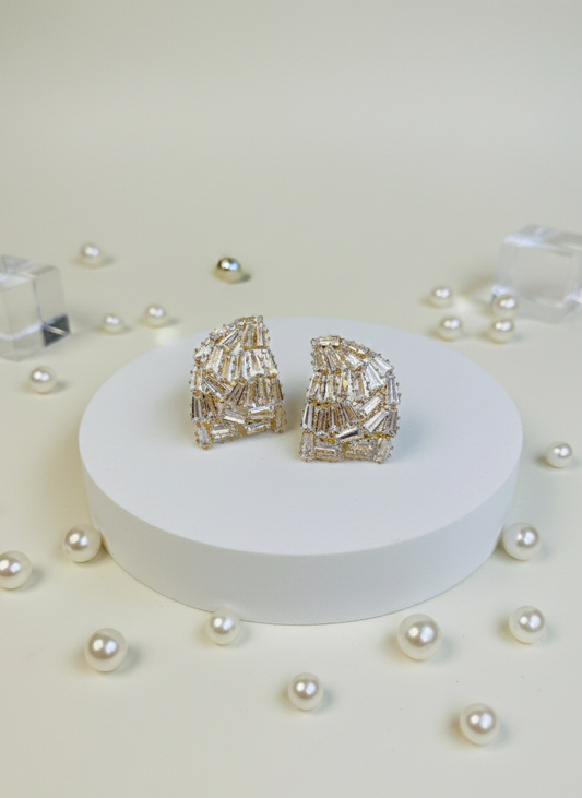 Pair of gold earrings on a white platform with scattered pearls on a light beige background