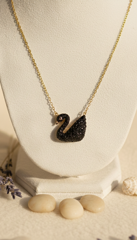 Black swan necklace on a white stand with stones and lavender flowers on a beige background