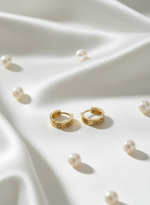 Gold hoop earrings with pearls on a white fabric background