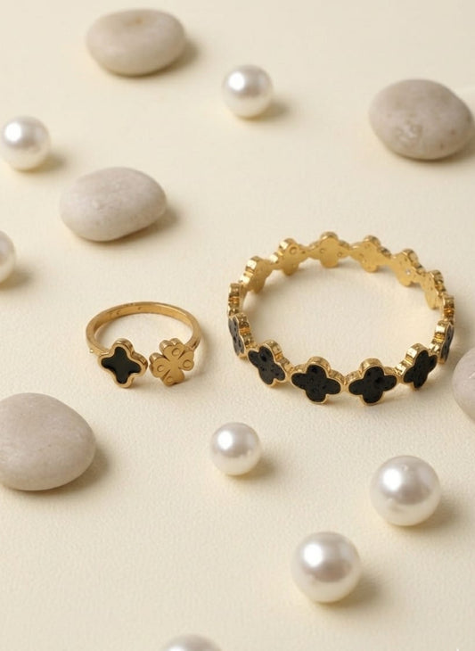 Gold rings with black accents on a beige surface with pearls and stones.