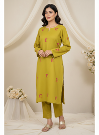 Woman wearing a green kurta with red patterns against a white curtain background