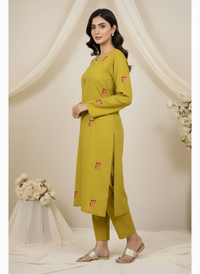 Woman wearing a mustard yellow kurta with pink patterns against a beige background