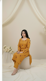 Woman in a mustard yellow dress sitting on a white stool against a white curtain background