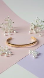 Gold bracelet on a pastel pink and purple background with small white flowers.