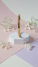 Gold ring on a white hexagonal stand with pearls on a pastel background