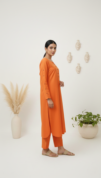 Woman wearing an orange outfit standing in a minimalistic room with plants and decor.
