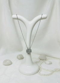 Silver necklace with a pendant on a white stand against a white background