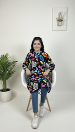 Woman sitting on a chair wearing a colorful patterned dress with a white background