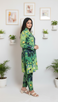 Woman wearing a green floral outfit standing in a room with plants and framed pictures on the wall.