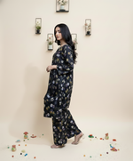 Woman wearing a dark floral outfit standing against a light beige wall with decorative elements.