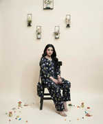 Woman sitting on a chair wearing a floral outfit with decorative elements on the floor.