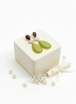 Pair of earrings with brown and orange stones on a white box with pearls around.