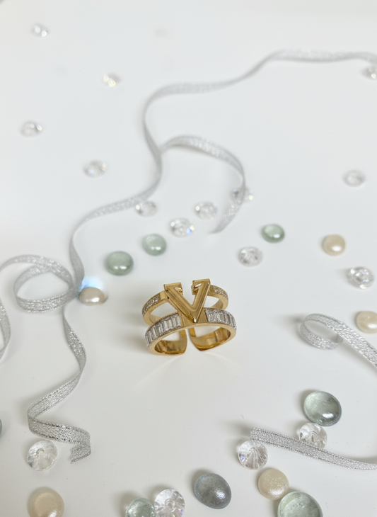 Gold ring with 'YV' design on a white background with ribbons and pearls