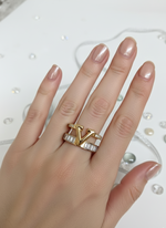 Hand wearing a gold ring with a 'V' design on a white background