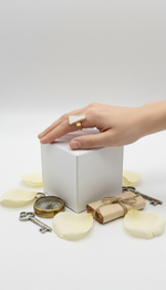 Hand holding a white cube with decorative items on a light background