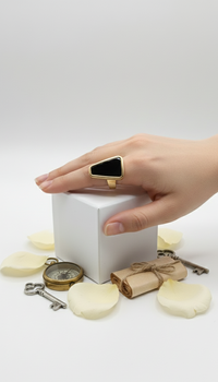Hand wearing a black triangle ring on a white cube with candles and keys on a light gray background