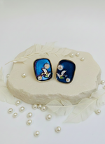 Pair of earrings with blue and black design on a white surface with pearls.