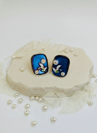 Pair of earrings with blue and black design on a white surface with pearls.