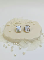 Pair of earrings on a decorative heart-shaped stand with pearls scattered around