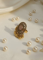 Gold ring with intricate design on a white, wavy surface