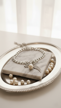 Silver bracelet with a feather charm on a marble surface with pearls.