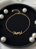 Gold bracelet with a unique design on a black dish surrounded by pearls.