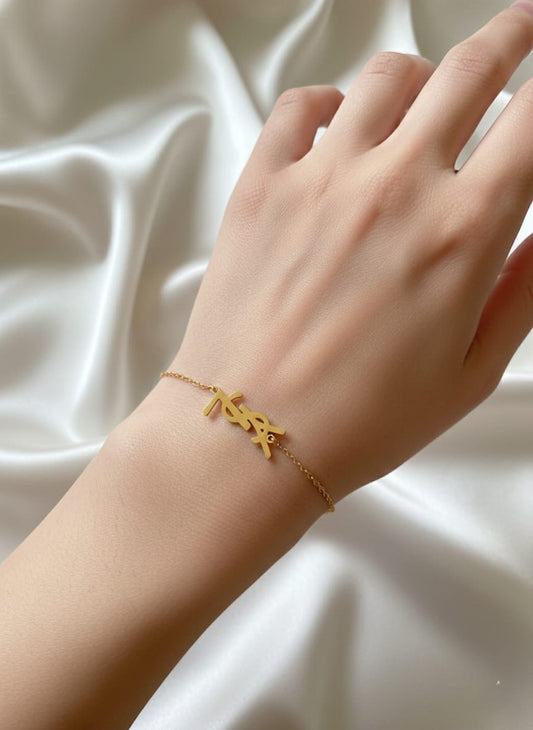 Gold bracelet with letter 'Y' on a hand against a white fabric background
